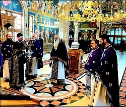 Група свештеника у љубичастој и црној одежди клечи у молитви на мермерном поду Храма Преображења Господњег на Златибору током Свете Тајне исповести свештенства. У фокусу је Часна Трпеза са црвеним покривачем и свећњацима, у дубоком ентеријеру храма са детаљним византијским фрескописом