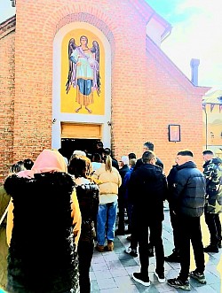 Odjeci liturgije: Pogled kroz otvorena vrata hrama ka porti crkve u Čajetini, gde se svetlost unutrašnjosti hrama stapa sa dnevnim svetlom, dok vernici izlaze ozareni nakon svete tajne, noseći mir u svoje domove i porodice