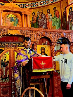 Седам православних свештенослужитеља из златиборског намесништва у саборном чину читања Светих Јеванђеља током Свете тајне јелеосвећења у храму Светог архангела Гаврила у Чајетини. Слика детаљно приказује свештенике из Сирогојна и Драглице како са страхом Божијим и дубоким пијететом припремају јеванђељске књиге за почетак молитве за здравље. Сваки од седам свештеника наизменично чита одељке који сведоче о Христовој моћи исцељења, док верни народ Чајетине и Златибора у потпуној тишини слуша речи спасења. Овај молитвени тренутак симболизује живу реч Божију која се излива на парохију чајетинску, призивајући благодат за све болесне и немоћне пред празник Васкрсења 2026. године